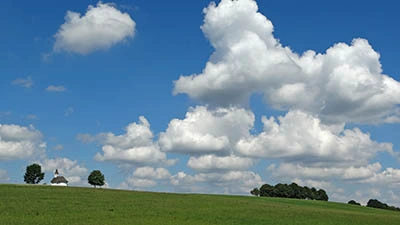 weiß-blauer Himmel über grüne Hügel